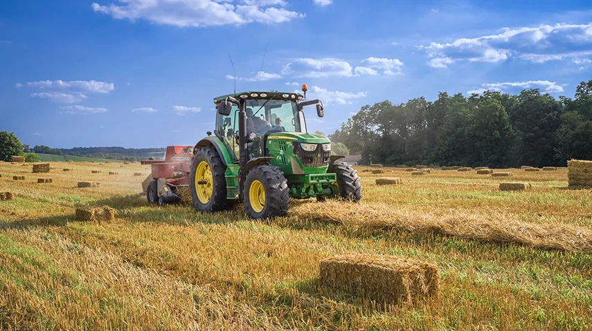 Farmer bailing hay on green tractor 
