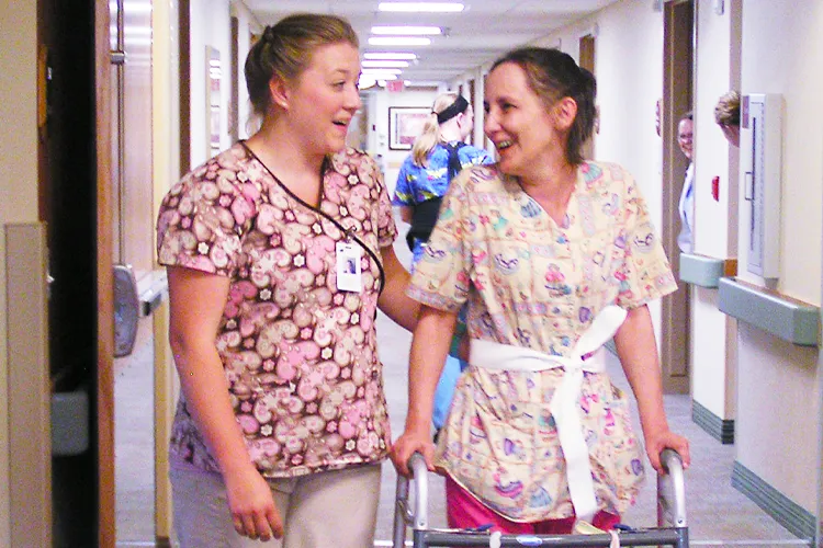 A CNA assists a patient walk down a hallway.