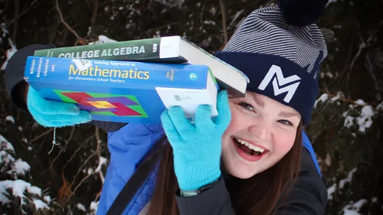 Student holding books in winter.