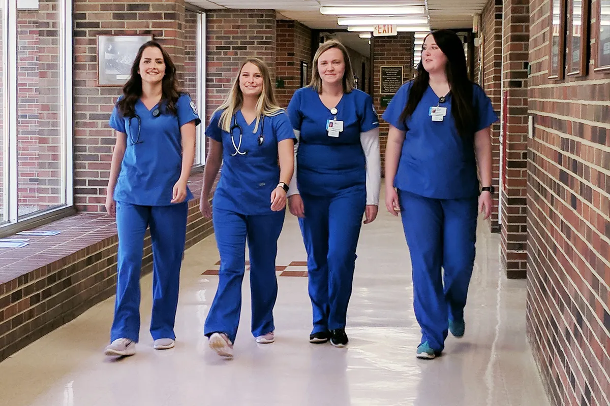 Four nursing students walk down a corridor.